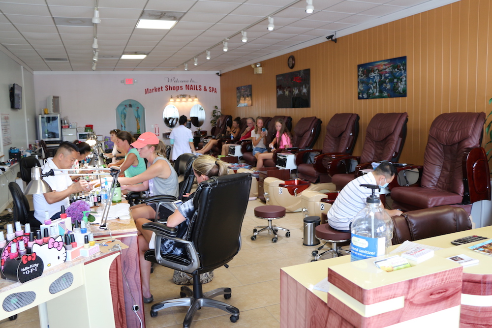 A manicure station next to a pedicure station with customers and employees at Market Shops Nails and Spa in Sandestin, Florida.