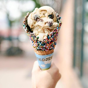 A person holding a waffle cone, dipped in chocolate and sprinkles, with Ben and Jerry's ice cream in it.